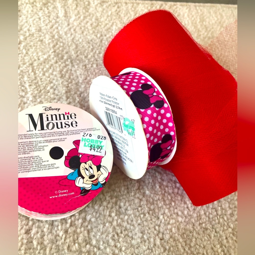 Two spools of pink Minnie Mouse ribbon. One large spool of red tulle.